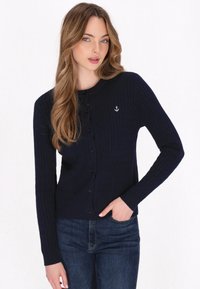 Marineblauwe geribde cardigan met lange mouwen, ronde halslijn, knopen aan de voorkant en een zilveren anker borduurdetail op de linkerkant van de borst.