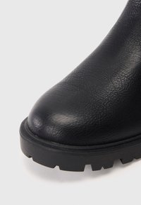 Sort læder ankelstøvle med en tekstureret overdel, rund tå og tyk, robust sål. Designet har ingen synlig hardware eller accenter.