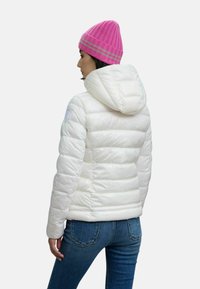Giacca bianca imbottita con cappuccio, caratterizzata da pannelli cuciti e una texture liscia. Abbinata a un berretto lavorato a maglia rosa con un motivo a coste.