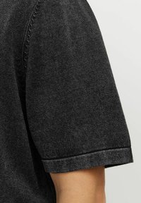 Chemise noire à manches courtes avec un tissu texturé, un col arrondi et des détails cousus sur les manches.