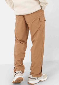 Cargo pants in lichtbruine stof, met zijzakken, een relaxte pasvorm en enkelritsen. Gecombineerd met wit en beige sneakers.