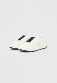 Λευκά παπούτσια τύπου slip-on από λείο υλικό, με μαύρη ελαστική ταινία, ανάγλυφο λογότυπο και υφασμένο ελαστικό πάτο.