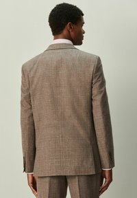 Braune kariertes Sakko mit strukturierter Stoffqualität, single Rücken-Schlitz und Revers mit Kerbkragen. Darunter ein helles Hemd getragen.