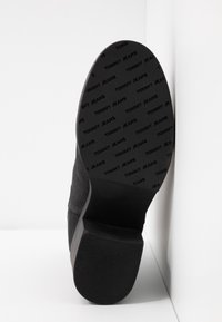 Mustat mokkanahkaiset nilkkurit, joissa on tekstuurilla varustettu kumipohja, jossa on painettu logodesign, sekä matala lohkokorko.