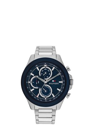 Orologio da polso in metallo argento con quadrante blu che mostra l'ora, la data, il giorno, i quadranti secondari delle 24 ore e le marcature del tachimetro, marca Hilfiger.