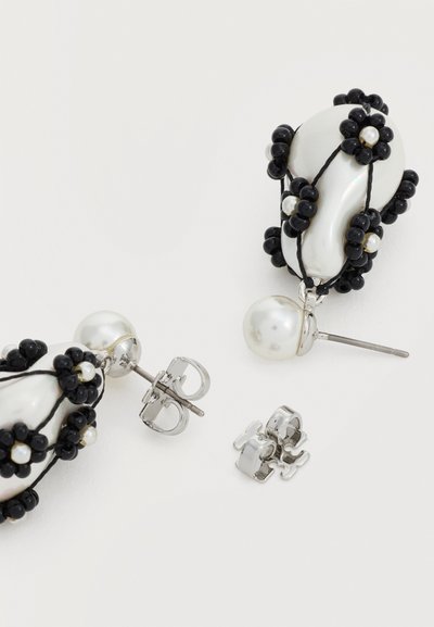 Boucles d'oreilles goutte avec des perles blanches irrégulières enveloppées de perles noires, attachées à de petits clous ronds en perle blanche avec fermoirs papillon.