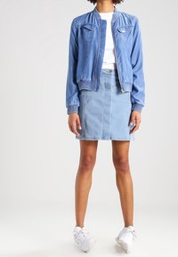 Vaaleansininen farkkupusakka, jossa on ribbireunukset, vetoketjukiinnitys ja kaksi etutaskua, yhdistettynä samansävyisiin farkkuhameeseen.