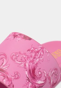 Pink slide sandal featuring a glossy finish, decorative swirl patterns, and a textured footbed. Bold brand name printed underneath.