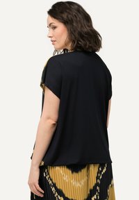 Černý top s krátkým rukávem a volným střihem; má kontrastní vzorovanou zadní část v žluté a černé barvě. Plisovaná sukně se podobným vzorem.