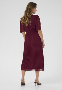 Maroon pleated midi dress with short, puffed sleeves and elastic waistband; smooth, flowing fabric; worn with heeled sandals.