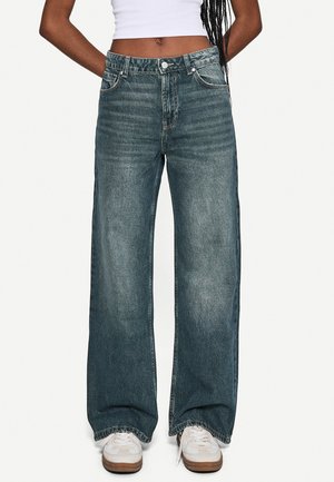 Bredde ben blå denimjeans med en falmet finish, fem lommer, sølvknap og lynlåslukning. Båret med beige sneakers.