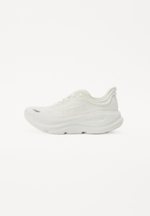 Chaussures de sport blanches avec une tige en mesh, une semelle épaisse et des détails texturés. Comprend des lacets et un logo sur le côté. Design arrondi.