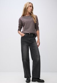 Gray wide-leg jeans with a high waist and pockets paired with a loose-fitting, muted purple long-sleeve top. Black ankle boots complete the look.