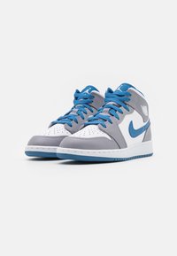 Baskets athlétiques montantes avec cuir gris clair, accents blancs, lacets bleus et swoosh bleu. Semelle texturée et bout perforé.