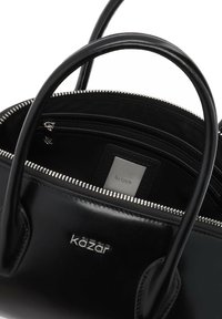 Crna kožna torba s dvostrukim ručkama, srebrnim zatvaračem i unutarnjim odjeljcima. Ima urezani logo i glatku teksturu.