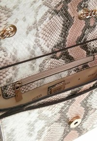 Sac à main en imprimé serpent avec quincaillerie métallique dorée. L'intérieur comprend une poche zippée et une doublure beige avec le logo de la marque. Détail de surface texturé.