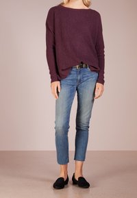 En vinröd stickad tröja med vid halsringning, kombinerad med ljusblå slim fit-jeans. Svarta slipskor fulländar outfiten.