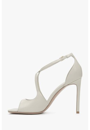 Light gray high-heeled sandals with open toe and ankle strap. Smooth leather texture, geometric cutouts, and a slender heel.