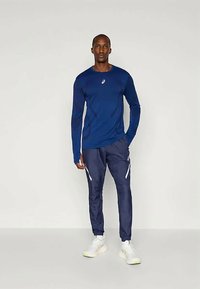 T-shirt de sport à manches longues bleu marine avec un design ajusté, associé à un pantalon de jogging bleu marine doté de poches zippées et d'accents réfléchissants.