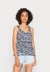 Top de tanque com padrão azul-marinho e alças com babados, decote em V e cintura elástica. Combinado com calções de ganga claros e desgastados.