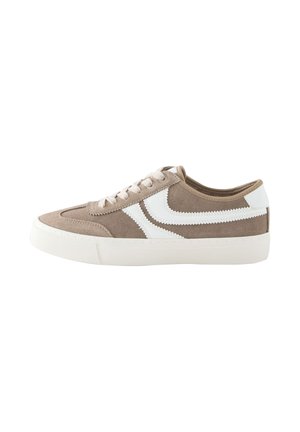 Pantof sport bej din piele întoarsă, cu dungi laterale albe în zigzag, talpă albă din cauciuc și șireturi bej, văzut din lateral pe fundal alb.