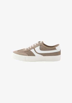 Beige suède lage sneaker met witte zigzag zijstrepen, witte rubberen zool en beige veters, gezien van opzij op een witte achtergrond.