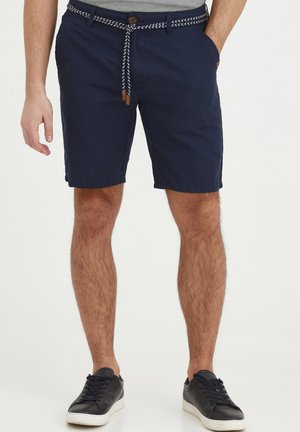 Pantaloni scurți de culoare bleu marin cu un șnur alb împletit, închidere cu nasture și buzunare laterale. Materialul pare ușor și comod.