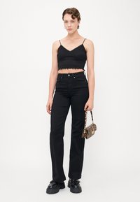 Čierny crop top s textúrovaným vzorom a volánikmi na leme, spárovaný s čiernymi vysokými džínsami, robustnými čiernymi topánkami a malou kabelkou s leopardím vzorom.