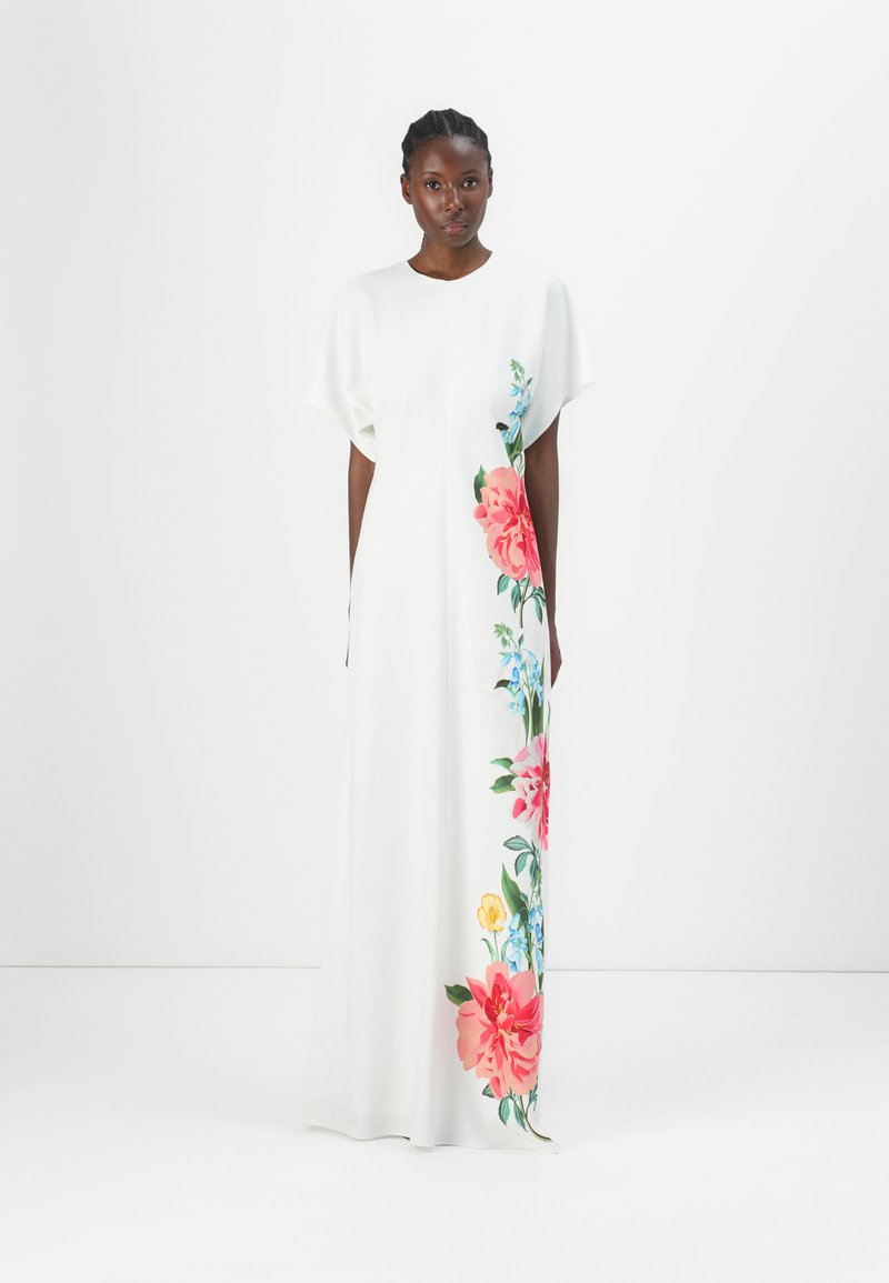 Robe maxi blanche avec une silhouette fluide, présentant un vibrant design floral en rose, bleu et jaune d'un côté. Texture de tissu lisse.