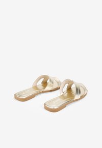 Sandalias planas metálicas doradas con dos correas cruzadas, tacón plano y plantilla de textura suave. Diseño ligero adecuado para el uso casual.
