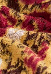 Vlnená tkanina s teplou farebnou paletou červenej, žltej a hnedej farby, s mäkkým, textúrovaným povrchom, ktorý zobrazuje odvážny abstraktný vzor.