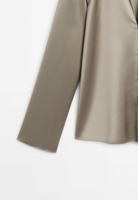 Manche longue en tissu lisse marron clair, affichée sur un fond blanc uni, montrant la manche et une partie du torse.