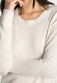 Pull en tricot beige clair avec un col rond classique, des manches longues et une texture douce et chaude. Subtiles variations dans l'épaisseur du fil.