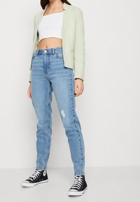 Jasnozielona marynarka na białym topie crop; niebieskie jeansy z wysokim stanem i przetarciami; czarne sneakersy za kostkę.