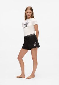Svarta shorts med elastisk midja, med en tecknad grafik på fållen. Matchas med en tight vit t-shirt som visar en liknande grafik.