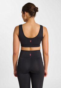 Svart sport-bh och höga leggings med midja, med ett slätt tyg, racerback-design och små röda triangeldetaljer på baksidan.