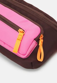 Borsa in tessuto marrone con una tasca con zip rosa. Presenta tirazip arancioni e cuciture in contrasto. Texture liscia, forma rettangolare.