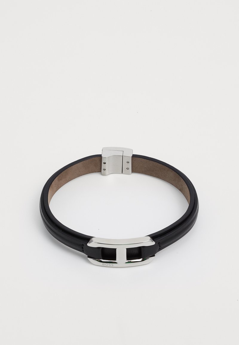 Mustmust nahkpael, millel on poleeritud hõbedane metallist lukuga, millel on pandla disain ja sile, tekstuuriga viimistlus sisetakendusel.