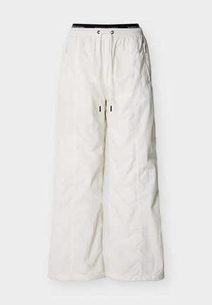 Λευκό παντελόνι με φαρδιά μπάλα, ελαστική μέση, κορδόνι και τσεπές στο πλάι με φερμουάρ, παρουσιάζεται σε απλό φόντο.