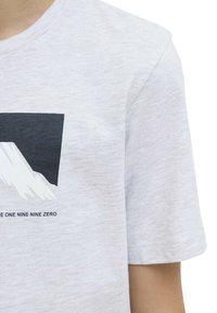 T-shirt gris clair à manches courtes en tissu doux, avec un graphique d'une montagne en noir et blanc et un texte en dessous.