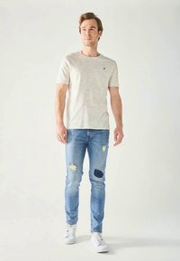 Lys grå kortermet t-skjorte med teksturert mønster, sammen med mellomblå skinny jeans med slitte detaljer og lapper.