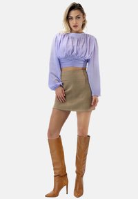 Lawendowa krótka bluzka z bufkowatymi rękawami, beżowa mini spódnica i wysokie brązowe botki na obcasie. Gładka tkanina o dopasowanym kroju.