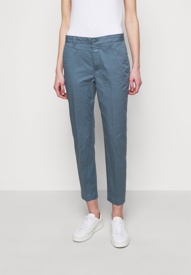 Chinos en azul claro con un diseño de pierna recta, confeccionados en suave tela de algodón. Presenta bolsillos frontales y cierre de botón. Combinados con zapatillas blancas.