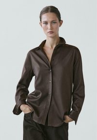 Camicia marrone a righe con maniche lunghe, colletto a punta e bottoni frontali, caratterizzata da una texture del tessuto liscia e vestibilità rilassata.