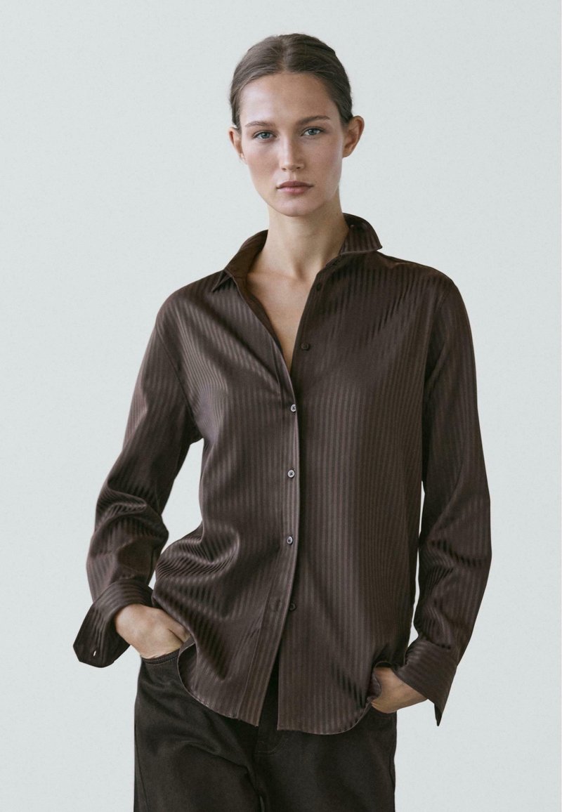 Camicia marrone a righe con maniche lunghe, colletto a punta e bottoni frontali, caratterizzata da una texture del tessuto liscia e vestibilità rilassata.