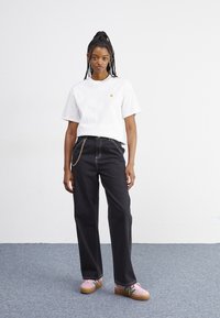 Λευκό βαμβακερό μπλουζάκι με μικρό κίτρινο λογότυπο, σε συνδυασμό με σκοτεινά τζιν παντελόνια με λεπτομέρεια αλυσίδας. Ροζ αθλητικά με πλατφόρμα και πράσινες λεπτομέρειες.