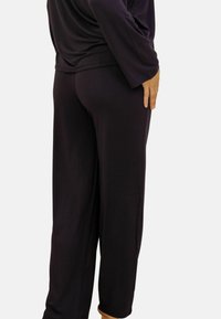Pantalons noirs amples en tissu doux, présentant un design à jambe droite et des poches sur les côtés, avec une texture lisse et un minimum de détails.