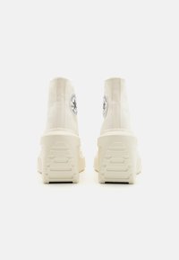 Høye sneakers i kremfarget lerret med en teksturert gummisåle. Har en sirkulær logopatch på utsiden og en forsterket hæl.
