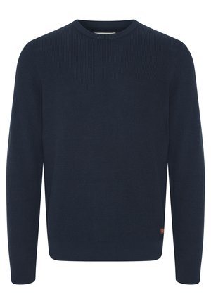 Maglione a coste blu navy con scollo rotondo. Maniche lunghe e dettagli sui fianchi. Piccola etichetta con logo marrone sull'orlo.