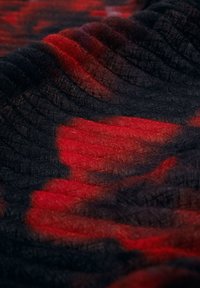 Sort og rød mønsterstof med en tekstureret vævning, der har et blødt, flydende udseende, der viser bølger af farver, der smelter sammen.